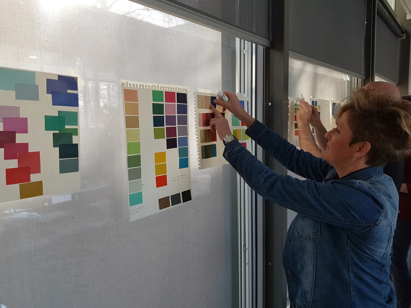 Cursiste wijst met een stift een kleurstaal aan op een kleurplan aan de wand